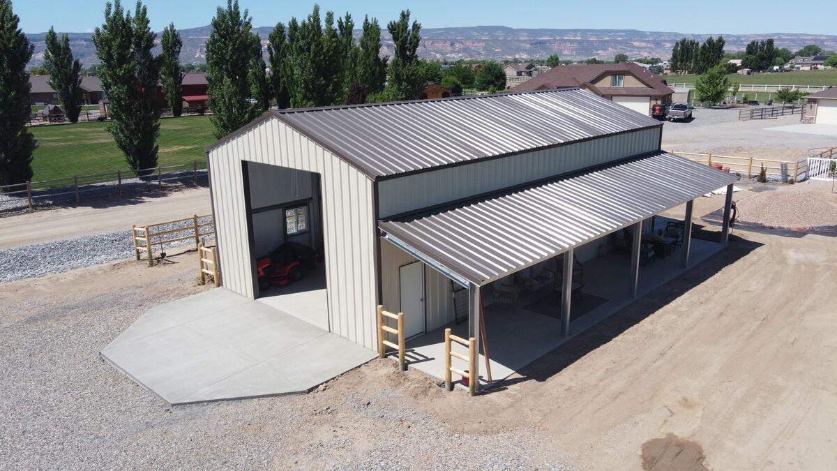 Steel equipment storage building with open lean-to and concrete pad on rural property
